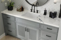 A close up of a gray vanity with reeded details on the doors and black hardware accents.