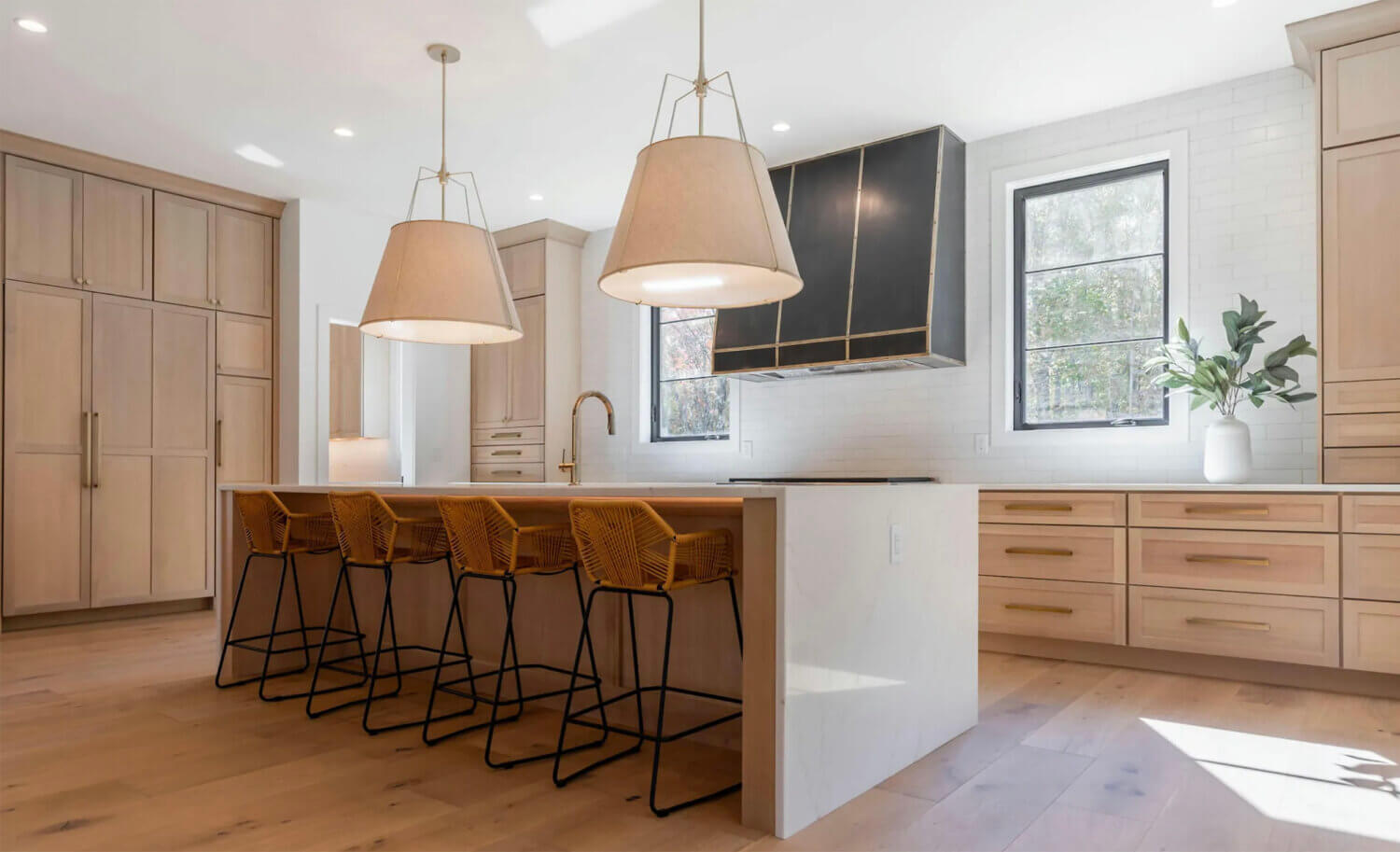 An extraordinary modern farmhouse kitchen design with qtr. sawn white oak cabinets with a light wood stain, a waterfall kitchen island and minimal wall cabinets.