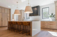 An extraordinary modern farmhouse kitchen design with qtr. sawn white oak cabinets with a light wood stain, a waterfall kitchen island and minimal wall cabinets.