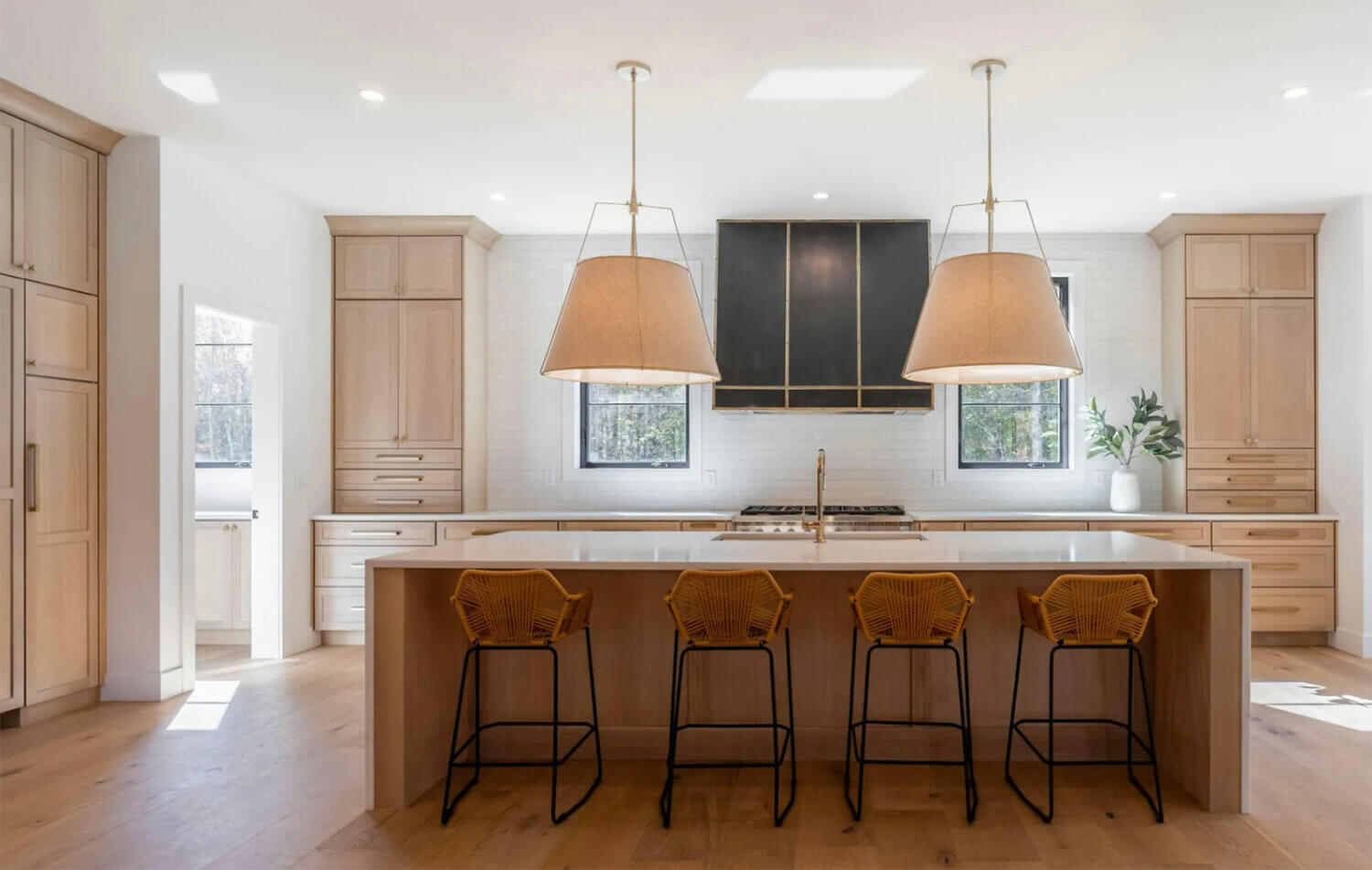 A beautiful all wood kitchen with quarter-sawn white oak cabinets with a soft, light stain color accented by golden satin brass pulls and hardware with a dark gray metal hood.