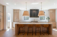 A beautiful all wood kitchen with quarter-sawn white oak cabinets with a soft, light stain color accented by golden satin brass pulls and hardware with a dark gray metal hood.