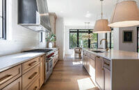 A stunning kitchen with light stained wood cabinets in White Oak with modern brassy accents and farmhouse styled pendant lights over the kitchen island.