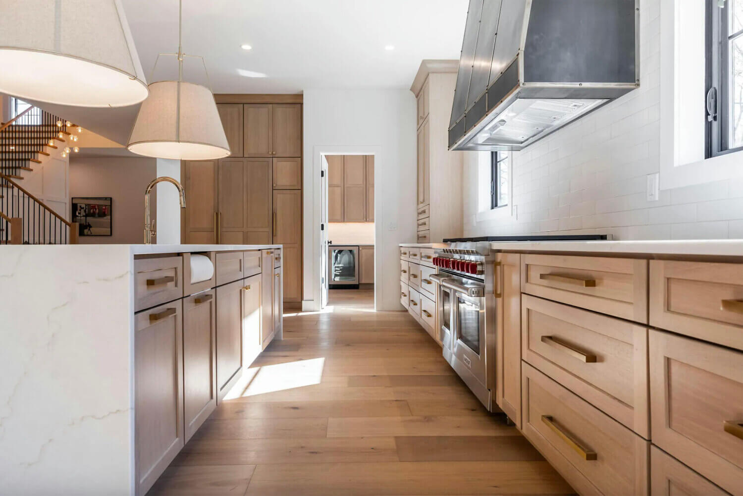 A trendy kitchen with light wood cabinets and wood flooring with an open concept layout and a large kitchen island with waterfall countertop and shaker cabinet doors.