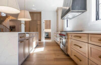 A trendy kitchen with light wood cabinets and wood flooring with an open concept layout and a large kitchen island with waterfall countertop and shaker cabinet doors.