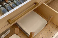 A wide drawer with a spice rack drawer above a deep kitchen drawer with a peg system organizer for plate and bowl storage.