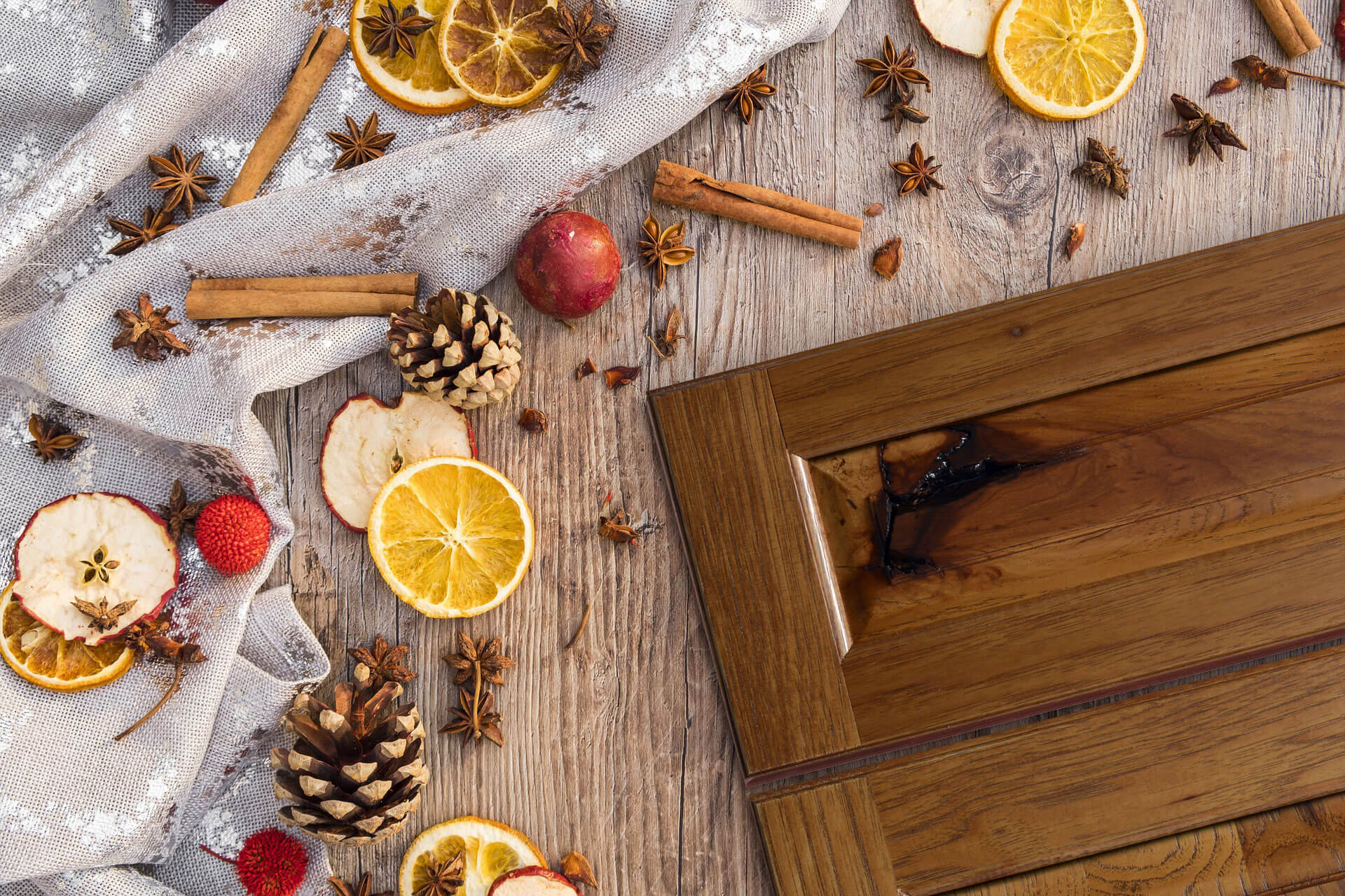 A flat panel cabinet door style with a delicious, red-orange stained finish on Rustic Hickory wood. Cinnamon sticks and apple cider supplies are scattered around the door on a table to emphasize the warm brown stain color with a subtle orange/red undertone.