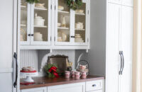A beautiful butler's pantry space with the kitchen fridge hidden behind appliance panels. The wire mesh cabinet doors are decorated for the holidays with small wreaths.