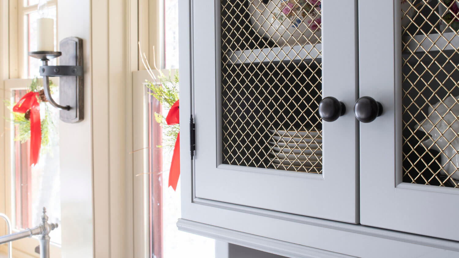 A close up of the light gray/off-white painted inset cabinet doors with chicken wire like wire mesh inserts.