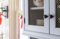 A close up of the light gray/off-white painted inset cabinet doors with chicken wire like wire mesh inserts.