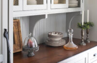 Gray painted inset cabinets with brushed brass wire mesh inserts decorative corbels and beadboard backsplash,