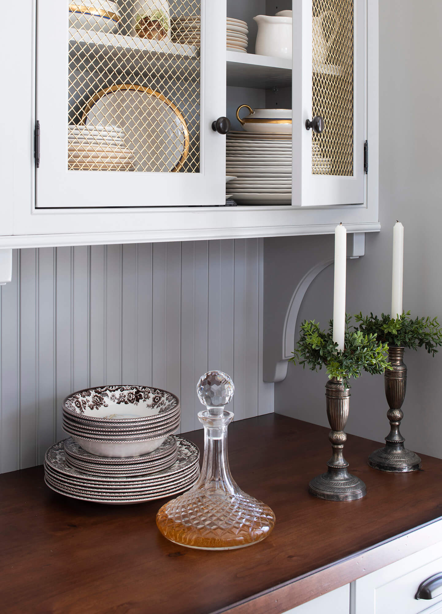 Inset cabinet doors with a gold wire mesh insert for storing decorative plateware and dishes.