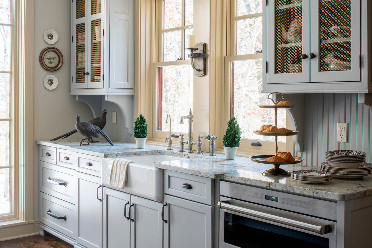 A beautiful butler's pantry with a large apron sink with a window view, gray cabinets and a beadboard backsplash for an Old English style look.
