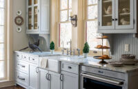 A beautiful butler's pantry with a large apron sink with a window view, gray cabinets and a beadboard backsplash for an Old English style look.