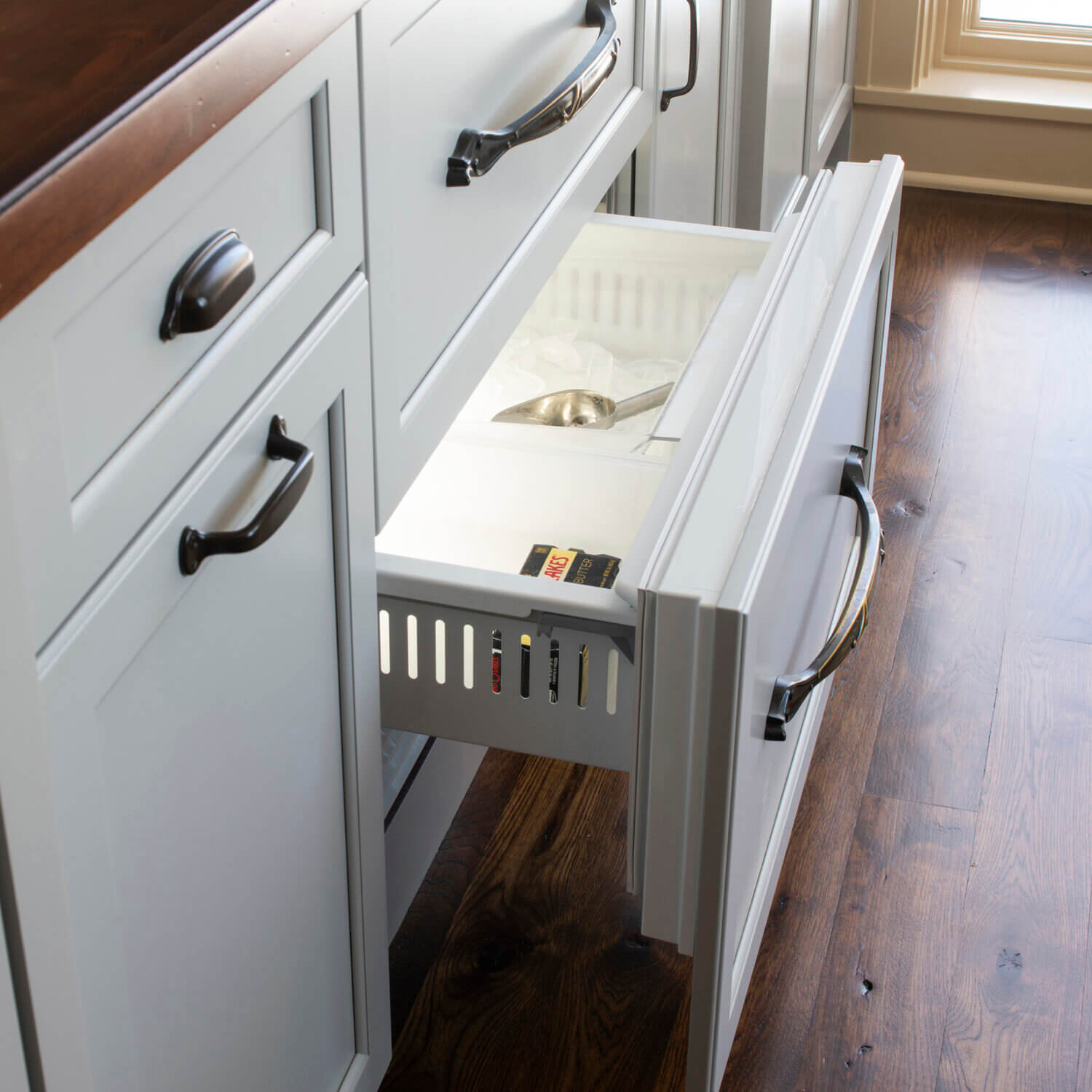 An ice drawer hidden behind cabinet appliance panel doors in an old English style butler's pantry.