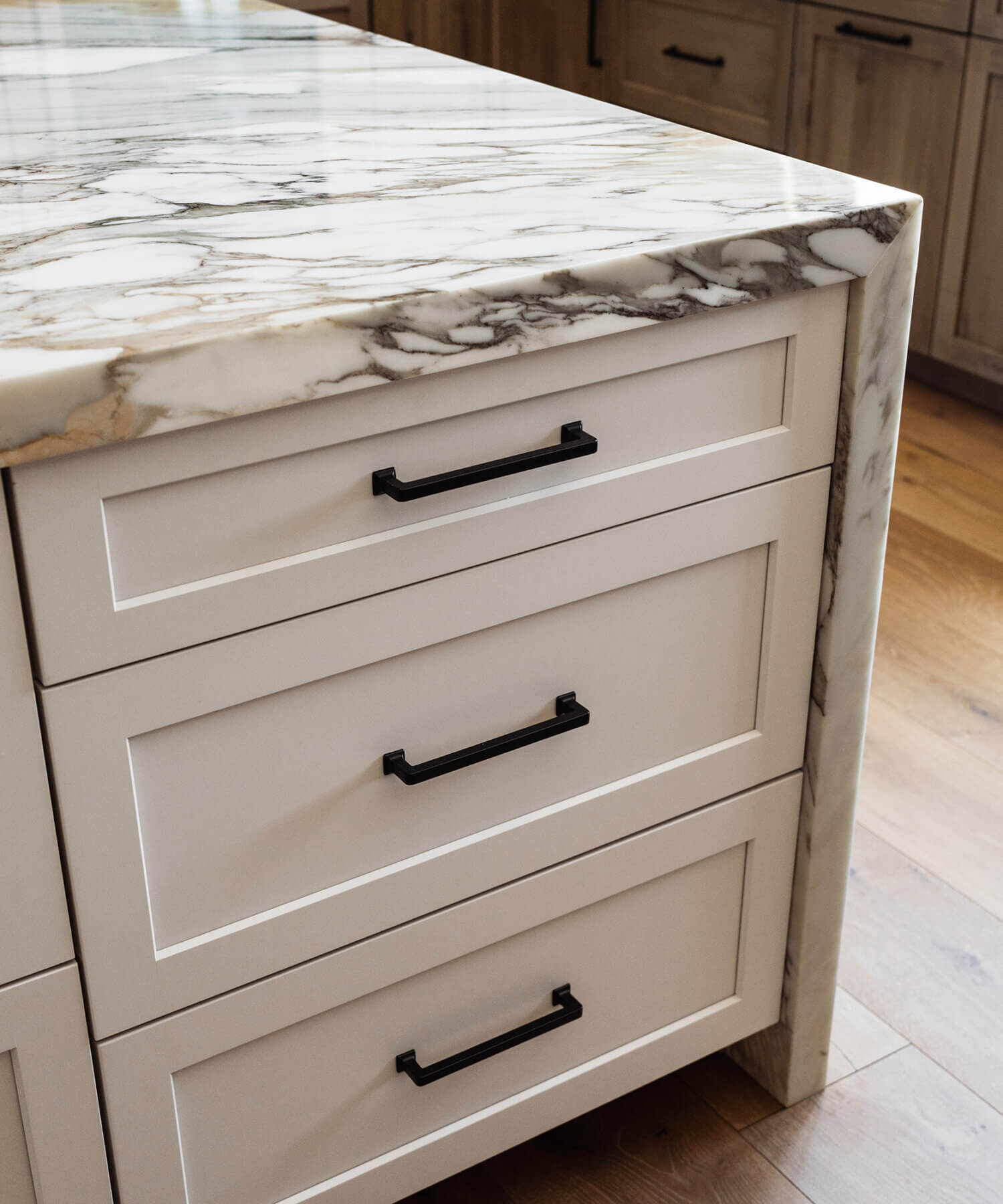 A close up of the kitchen island cabinets with a waterfall countertop and Putty paint (an off-white paint color) cabinets in a shaker door style.