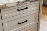 A close up of the kitchen island cabinets with a waterfall countertop and Putty paint (an off-white paint color) cabinets in a shaker door style.
