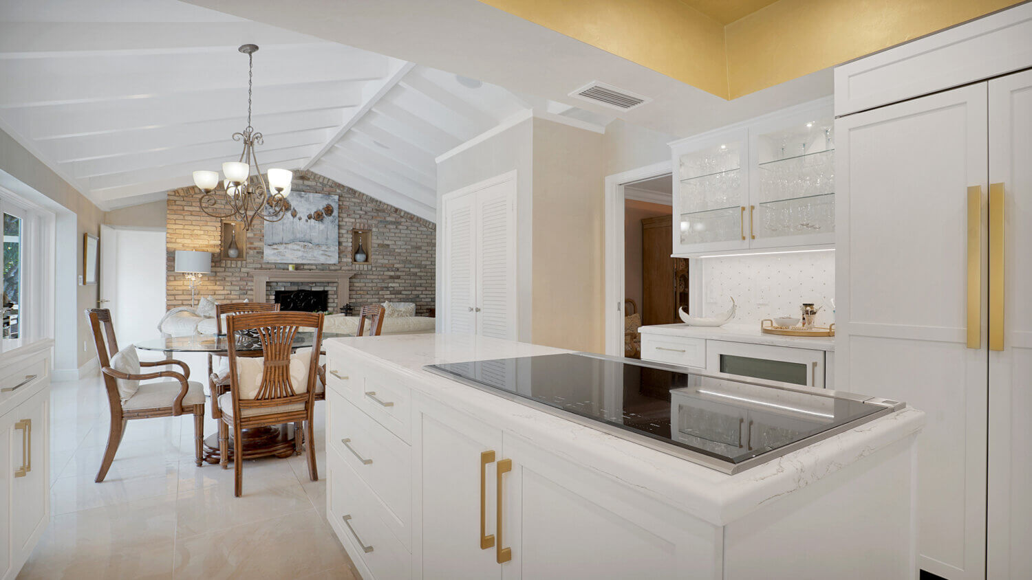 This bright white kitchen features Dura Supreme Cabinetry’s Homestead Panel door style in “White” paint paired with white countertops & backsplash with a golden ceiling and gold hardware pulls.