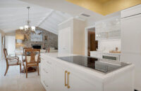 This bright white kitchen features Dura Supreme Cabinetry’s Homestead Panel door style in “White” paint paired with white countertops & backsplash with a golden ceiling and gold hardware pulls.