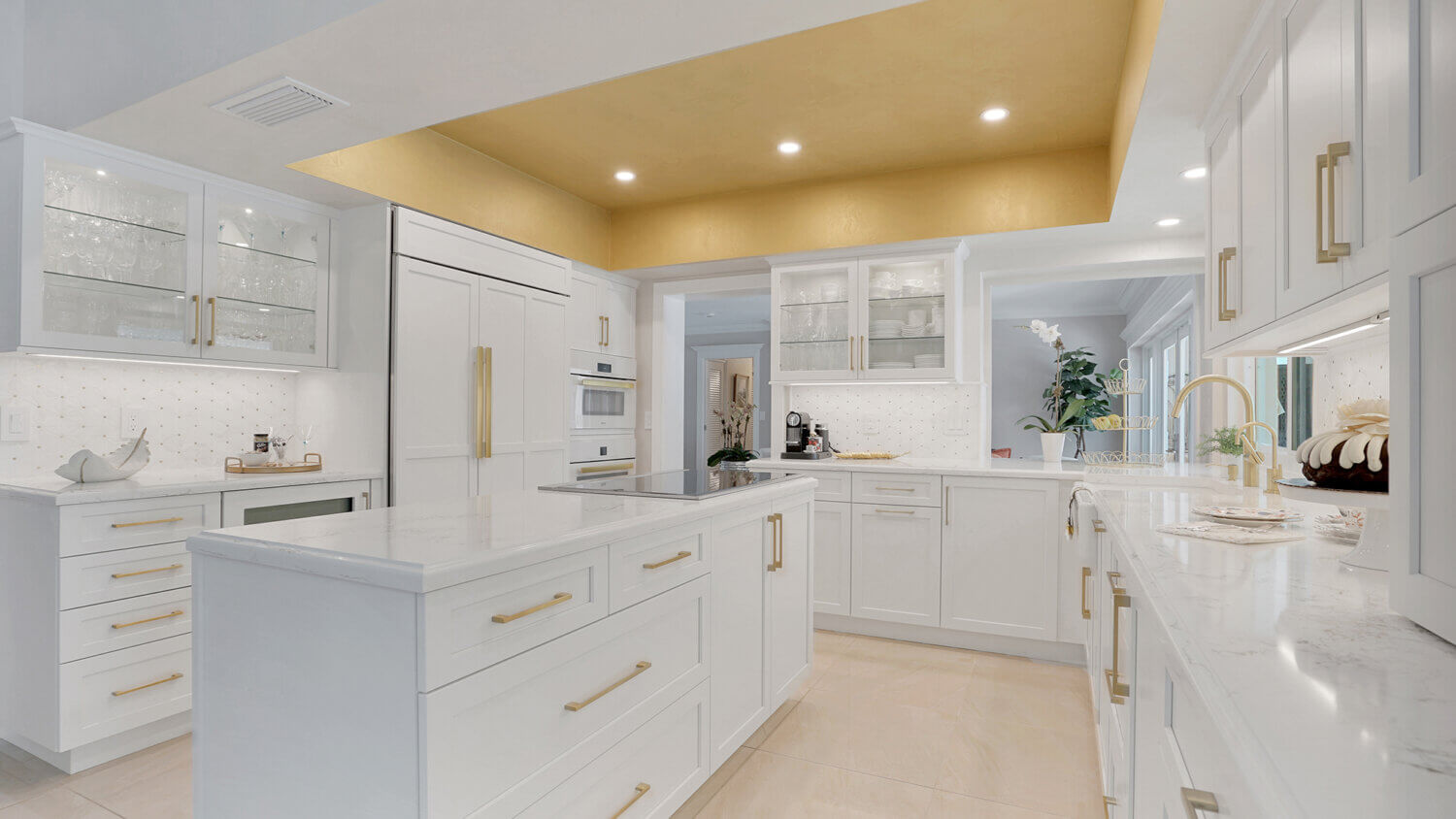 This bright white kitchen features Dura Supreme Cabinetry’s Homestead Panel door style in “White” paint paired with white countertops & backsplash with a golden ceiling and gold hardware pulls.