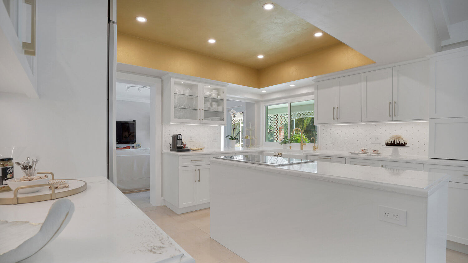 This bright white kitchen features Dura Supreme Cabinetry’s Homestead Panel door style in “White” paint paired with white countertops & backsplash with a golden ceiling and gold hardware pulls.