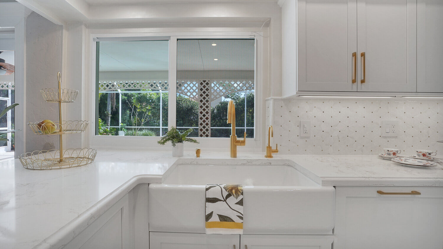 This bright white kitchen features Dura Supreme Cabinetry’s Homestead Panel door style in “White” paint paired with white countertops & backsplash with a golden ceiling and gold hardware pulls.