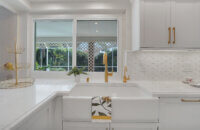 This bright white kitchen features Dura Supreme Cabinetry’s Homestead Panel door style in “White” paint paired with white countertops & backsplash with a golden ceiling and gold hardware pulls.