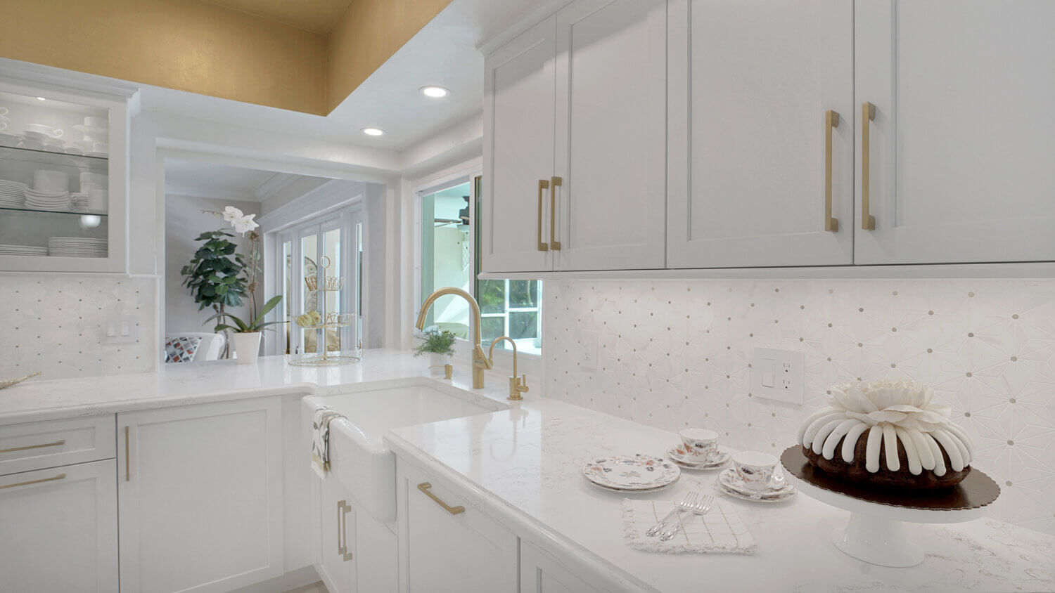 This bright white kitchen features Dura Supreme Cabinetry’s Homestead Panel door style in “White” paint paired with white countertops & backsplash with a golden ceiling and gold hardware pulls.