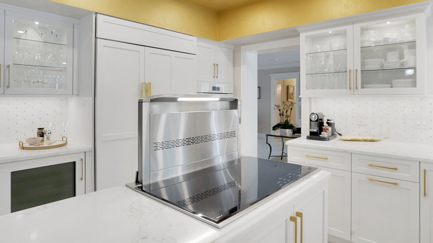 This bright white kitchen features Dura Supreme Cabinetry’s Homestead Panel door style in “White” paint paired with white countertops & backsplash with a golden ceiling and gold hardware pulls.