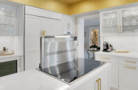 This bright white kitchen features Dura Supreme Cabinetry’s Homestead Panel door style in “White” paint paired with white countertops & backsplash with a golden ceiling and gold hardware pulls.