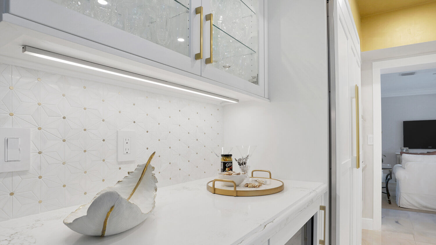 This bright white kitchen features Dura Supreme Cabinetry’s Homestead Panel door style in “White” paint paired with white countertops & backsplash with a golden ceiling and gold hardware pulls.