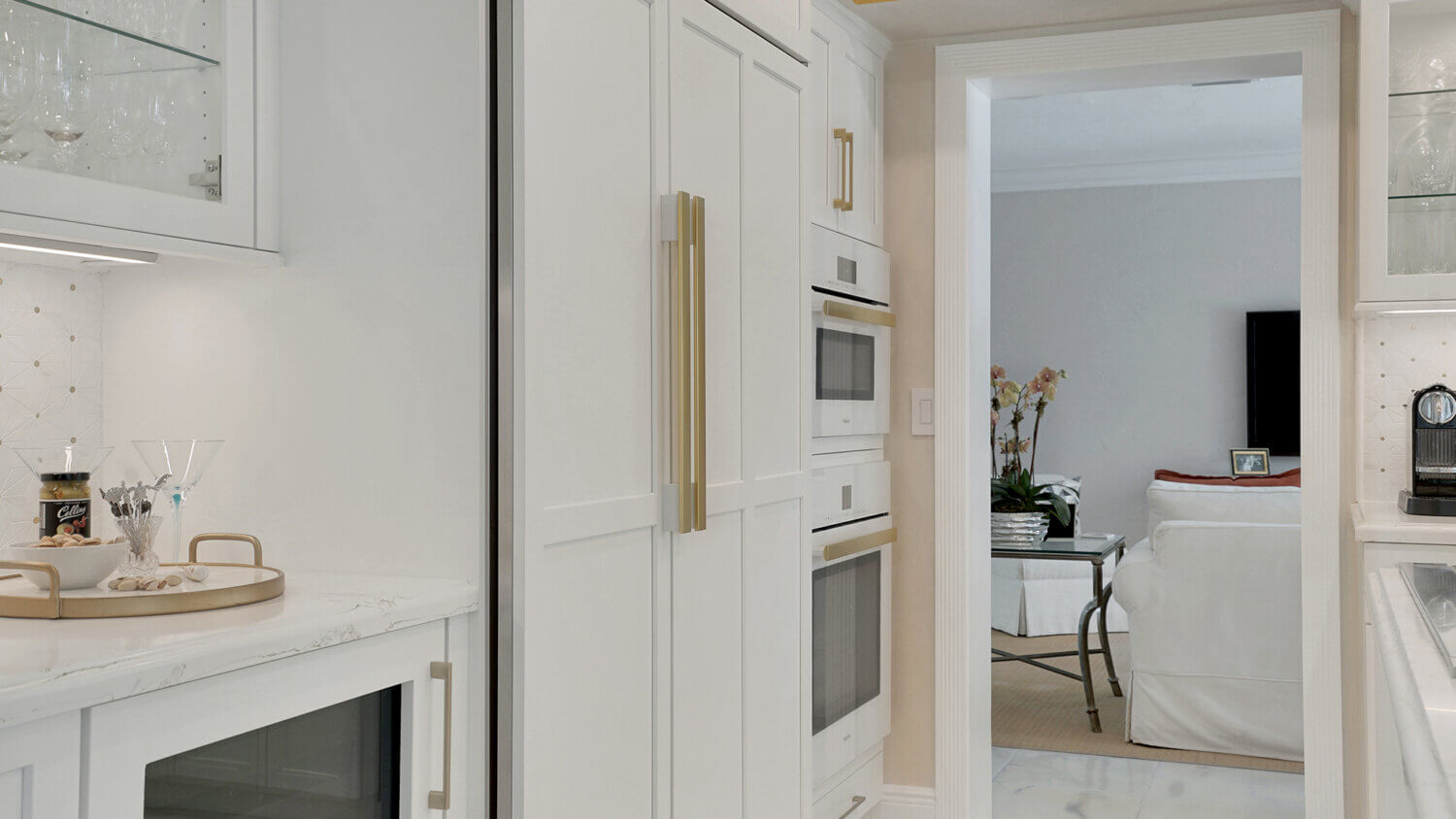 This bright white kitchen features Dura Supreme Cabinetry’s Homestead Panel door style in “White” paint paired with white countertops & backsplash with a golden ceiling and gold hardware pulls.