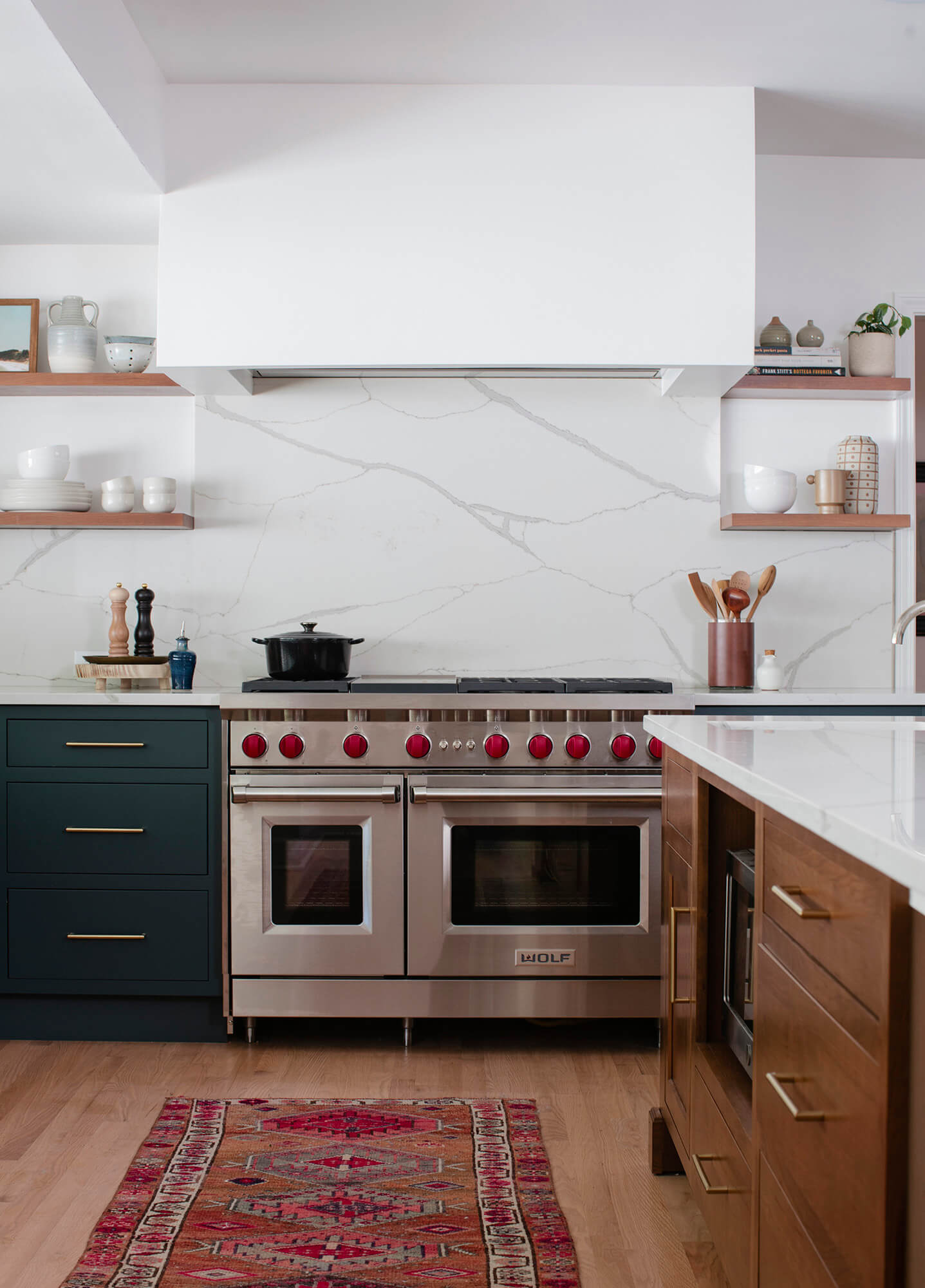 This kitchen is a great example of the latest trend of deep, earthy green cabinetry. Green is the color of nature, and it symbolizes growth, harmony, freshness, and fertility. This kitchen showcases Dura Supreme Cabinetry with the Homestead Panel Inset door style with optional solid slab drawer fronts in a combination of the “Rock Bottom” painted finish (perimeter cabinets) and the “Toast” stain on Cherry (kitchen island & floating shelves).