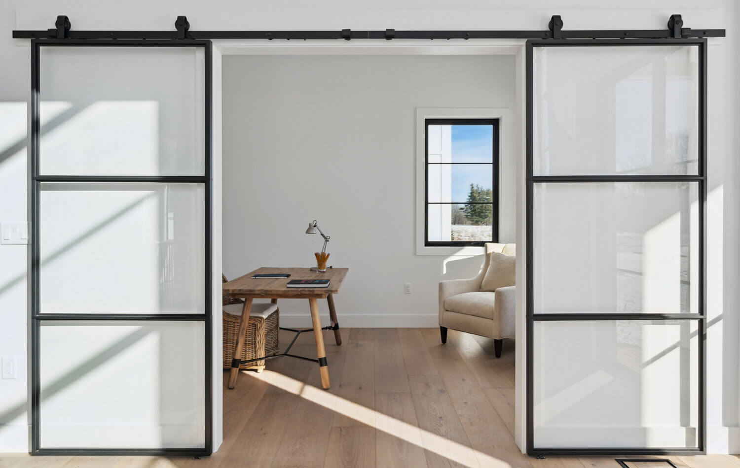 Sliding black metal barn style doors with glass panels slide open to reveal the modern home office space.