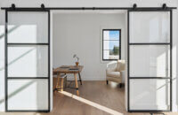 Sliding black metal barn style doors with glass panels slide open to reveal the modern home office space.