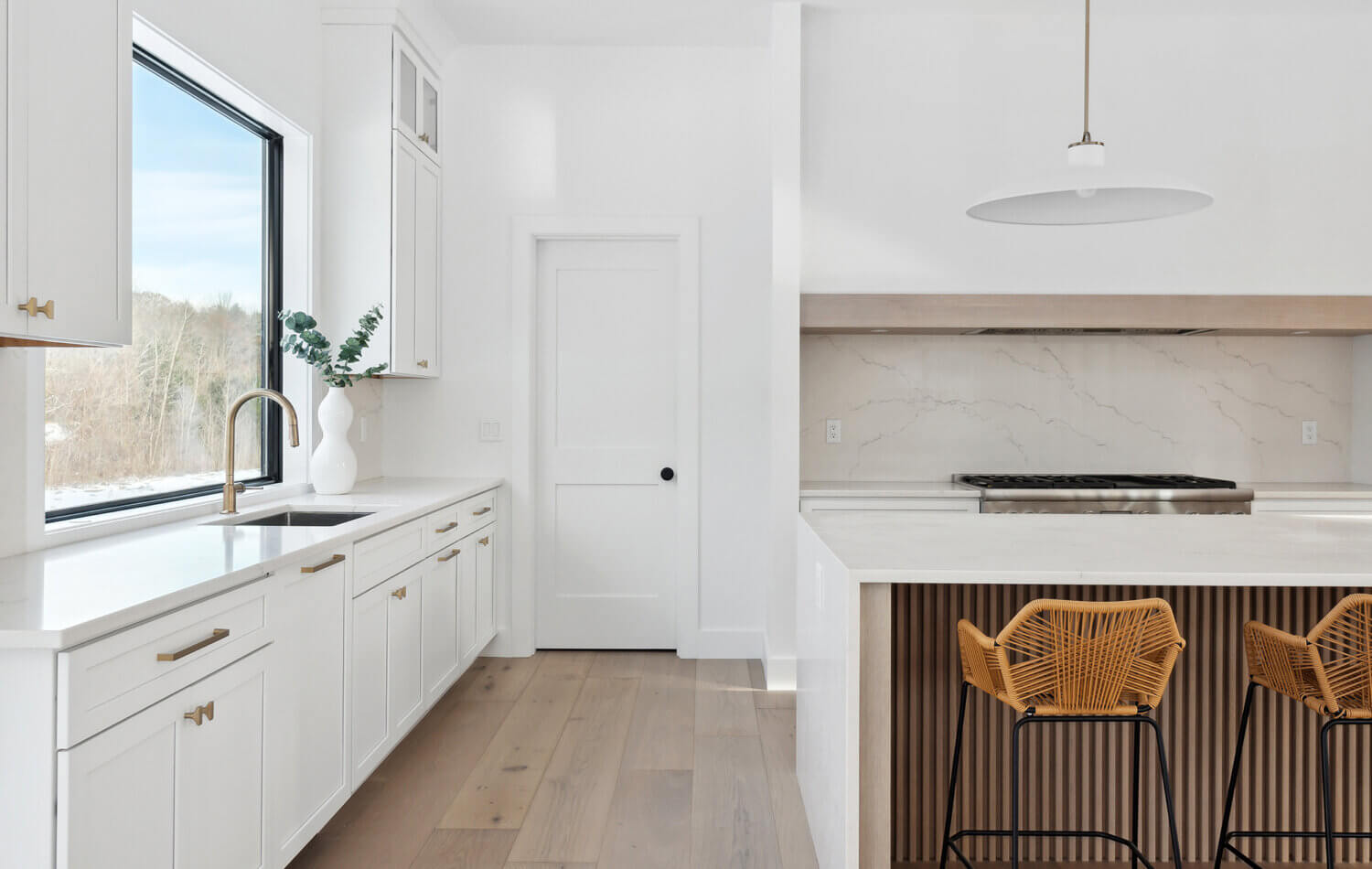A bright white modern farmhouse kitchen design with white painted cabinets and a fluted light wood stained kitchen island, waterfall countertops, and a range alcove space.