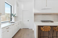 A bright white modern farmhouse kitchen design with white painted cabinets and a fluted light wood stained kitchen island, waterfall countertops, and a range alcove space.