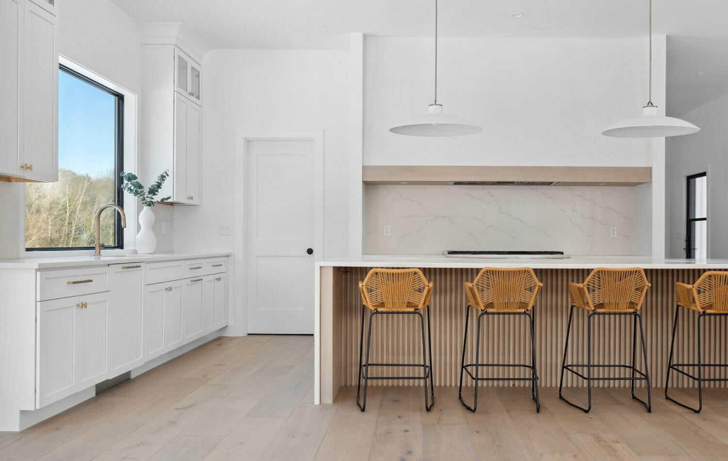 A stunning modern farmhouse kitchen with a wide range alcove space with a simple raw-wood panel mantel over the range. The island features custom fluted details to accent the seating area while waterfall countertops frame the island.