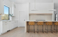 A stunning modern farmhouse kitchen with a wide range alcove space with a simple raw-wood panel mantel over the range. The island features custom fluted details to accent the seating area while waterfall countertops frame the island.