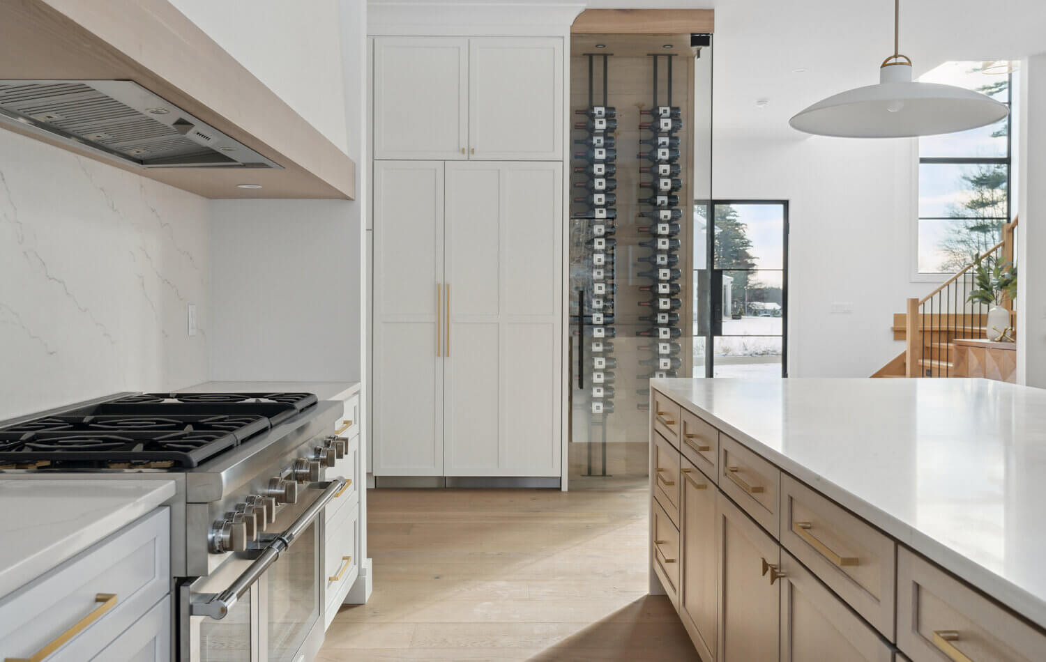 A luxurious modern farmhouse design with a range alcove, a light wood kitchen island, and a wine bottle wall behind glass.