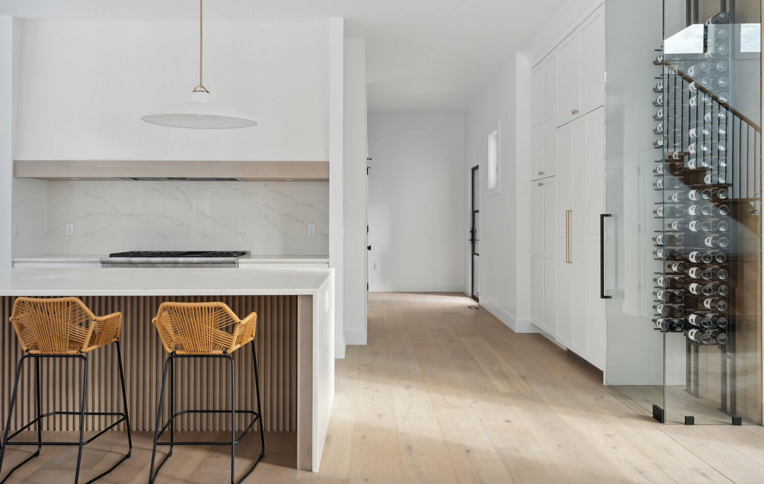 A stunning modern farmhouse kitchen with a wide range alcove space with a simple raw-wood panel mantel over the range. The island features custom fluted details to accent the seating area while waterfall countertops frame the island.