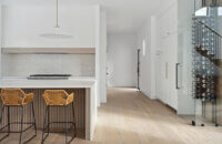 A stunning modern farmhouse kitchen with a wide range alcove space with a simple raw-wood panel mantel over the range. The island features custom fluted details to accent the seating area while waterfall countertops frame the island.