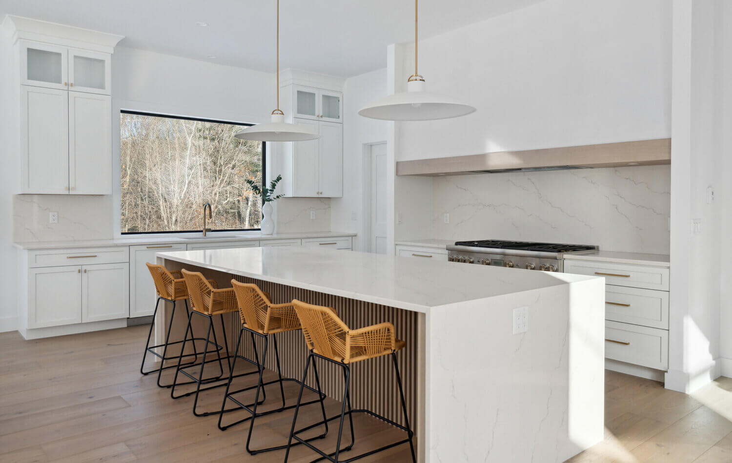 A stunning modern farmhouse kitchen with a wide range alcove space with a simple raw-wood panel mantel over the range. The island features custom fluted details to accent the seating area while waterfall countertops frame the island.