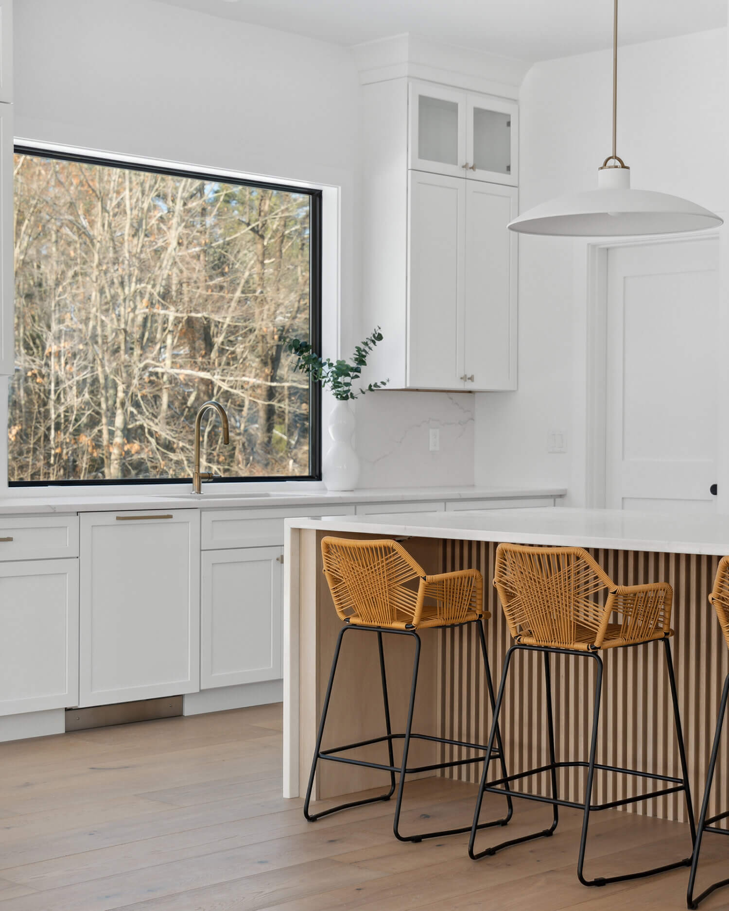 A trendy, modern farmhouse styled kitchen with wide, black industrial windows, white painted cabinets, and an organic, natural wood kitchen island with a grooved kitchen island panel featuring a fluted look.