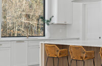 A trendy, modern farmhouse styled kitchen with wide, black industrial windows, white painted cabinets, and an organic, natural wood kitchen island with a grooved kitchen island panel featuring a fluted look.