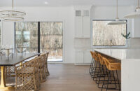 A stunning modern farmhouse kitchen with a wide range alcove space with a simple raw-wood panel mantel over the range. The island features custom fluted details to accent the seating area while waterfall countertops frame the island.