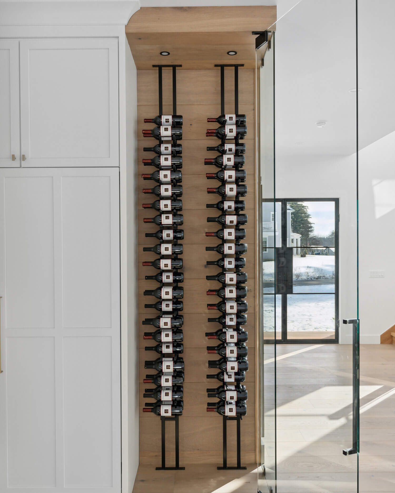 A floor-to-ceiling wine rack wall behind glass. The wine storage is accented with light stained quarter-sawn white oak wood that beautifully contrasts the white painted cabinets throughout the kitchen.