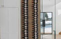 A floor-to-ceiling wine rack wall behind glass. The wine storage is accented with light stained quarter-sawn white oak wood that beautifully contrasts the white painted cabinets throughout the kitchen.