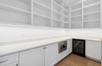 The walk in pantry is all white with open wall cabinet shelves for easy access and checking inventory of kitchen goods and supplies.