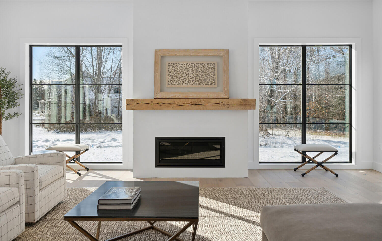 A simple fireplace mantel in a modern farmhouse living room. surrounded by large black framed windows with an industrial style.