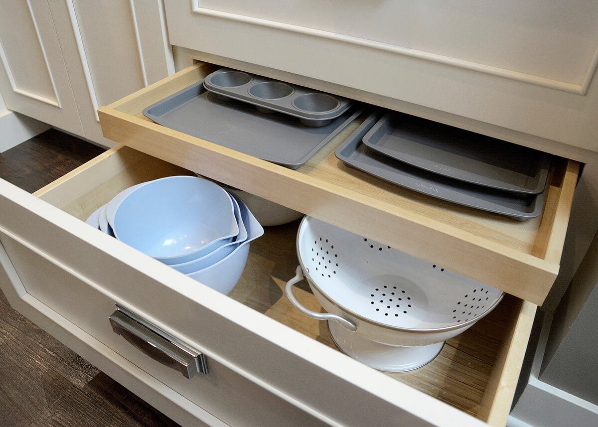 A Shallow Roll-Out from Dura Supreme Cabinetry in a deep drawer neatly stores your pans, trays, and cookie sheets in the same drawer as your mixing bowls.